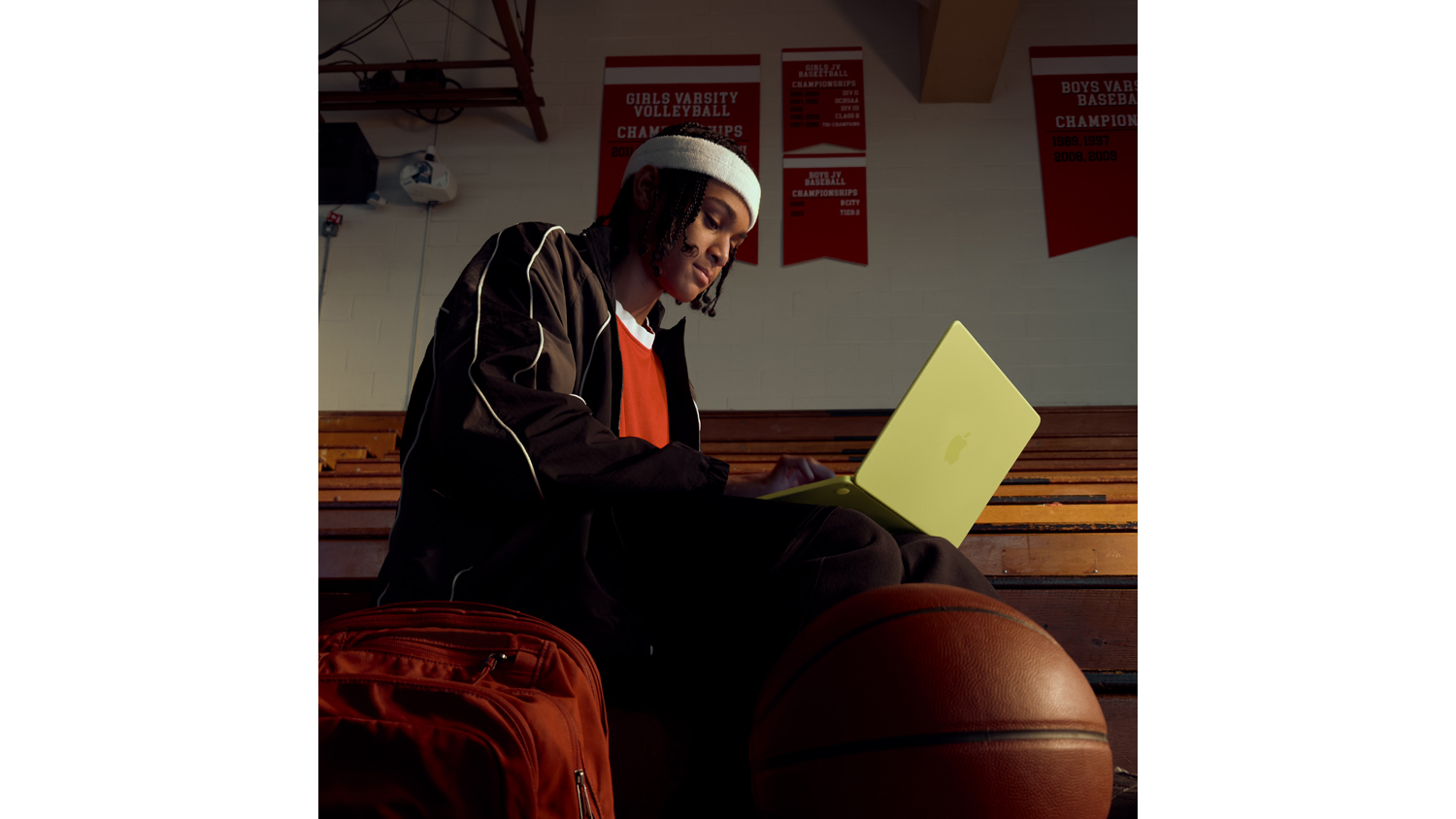A person sitting on a basketball with a MacBook Neo, showcasing its portability for students
