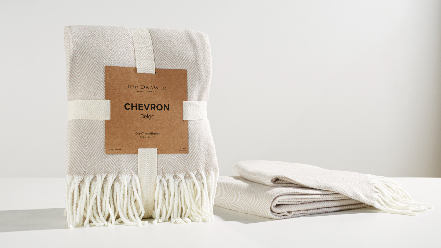 Chevron Beige Throw by Top Drawer, standing neatly folded, and a second folded throw lies beside it