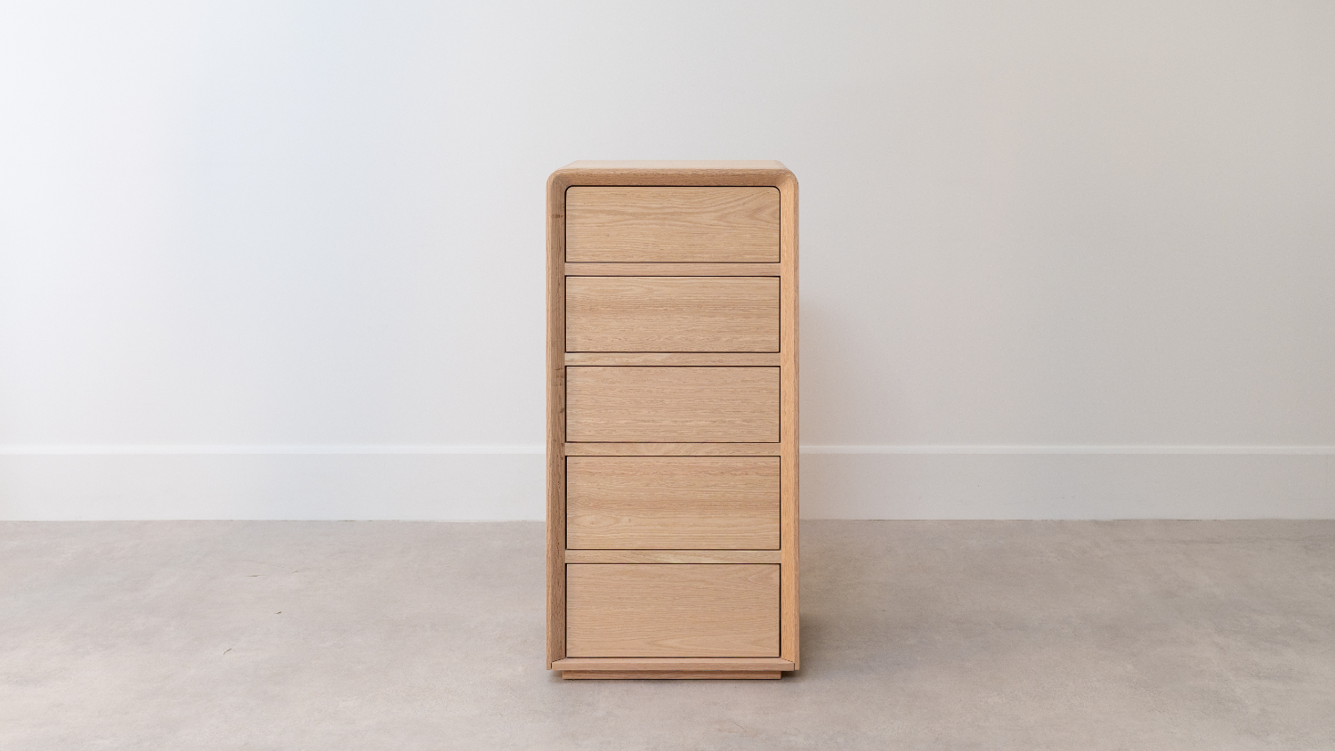 Front of a slim, tall wooden five‑drawer tallboy with a smooth, rounded‑edge frame and flat drawer fronts