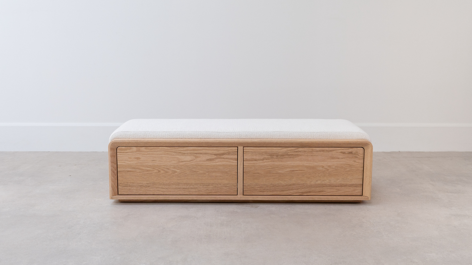 A low, rectangular wooden bed‑end chest with two wide front drawers and a padded light‑fabric top