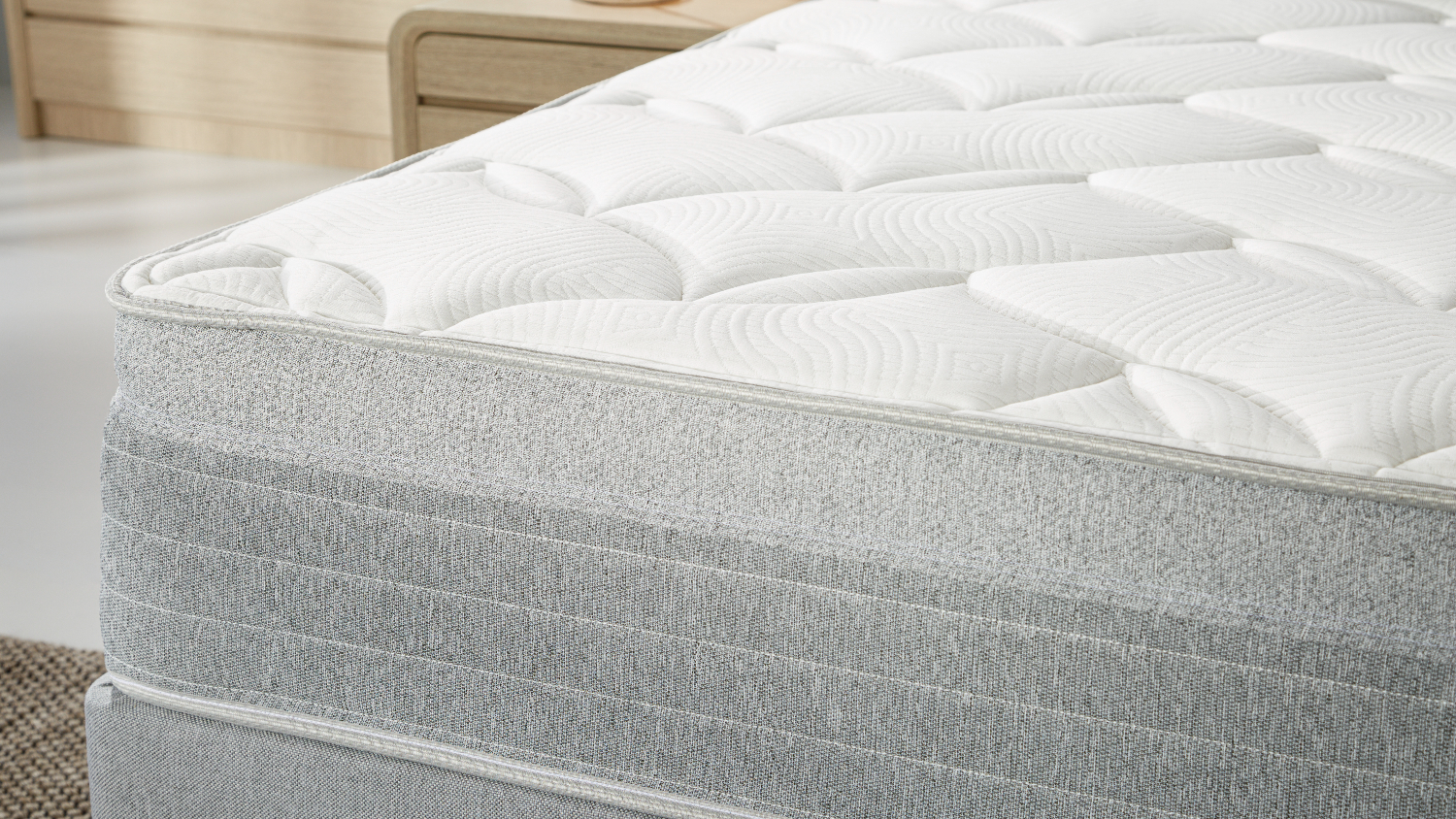 Side close‑up of the mattress edge, focusing on the soft quilted top layer and textured grey fabric