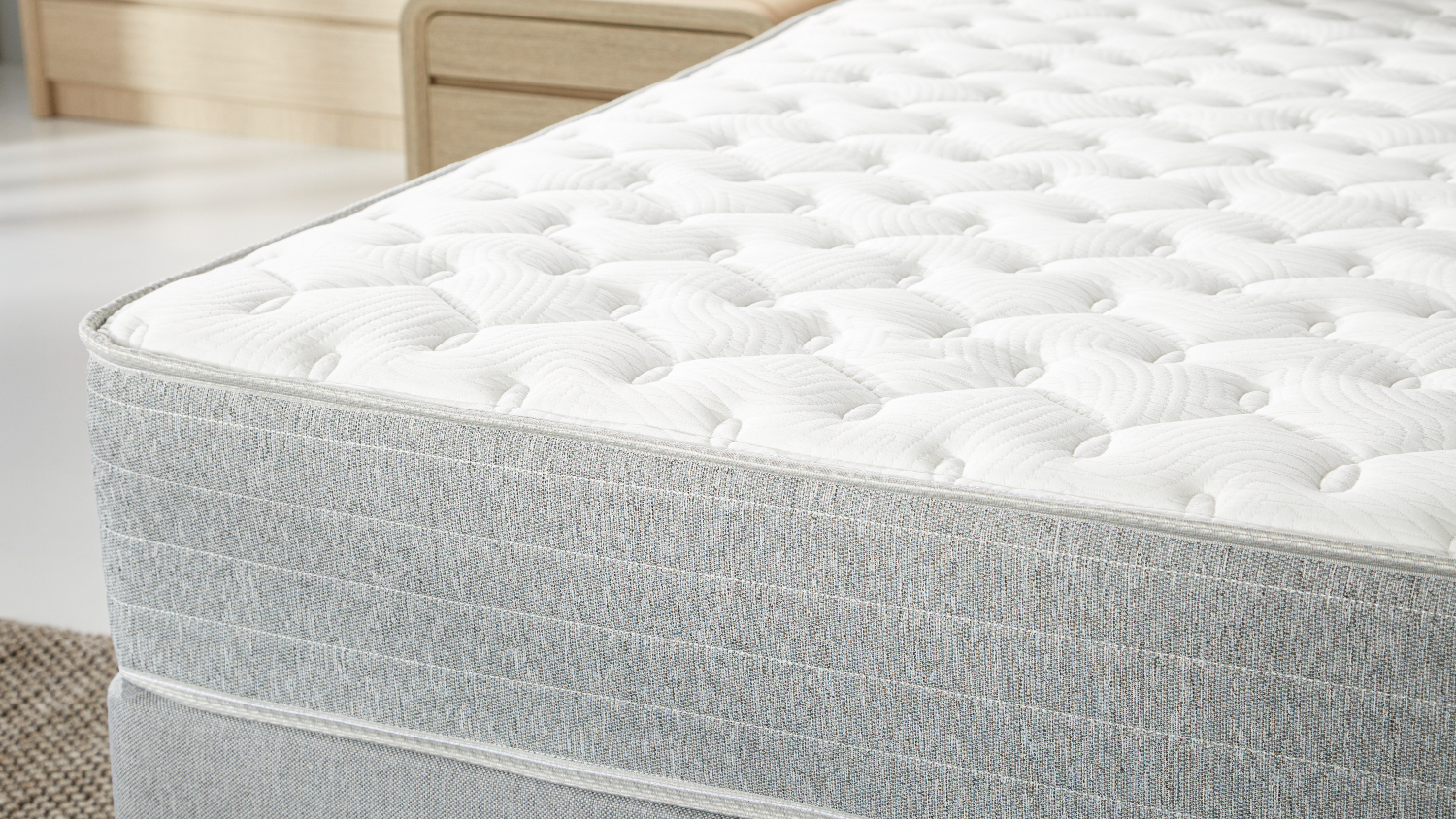 Side close‑up of the mattress edge, focusing on the quilted top layer and textured grey fabric