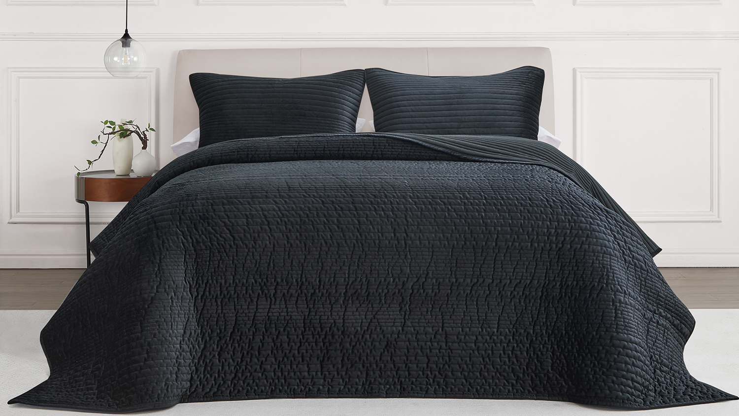 Front view of a neatly styled bed dressed in a black ruched velvet queen coverlet set