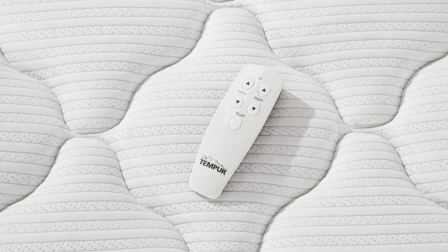 Top‑down close‑up of a white Tempur remote control resting on the mattress surface