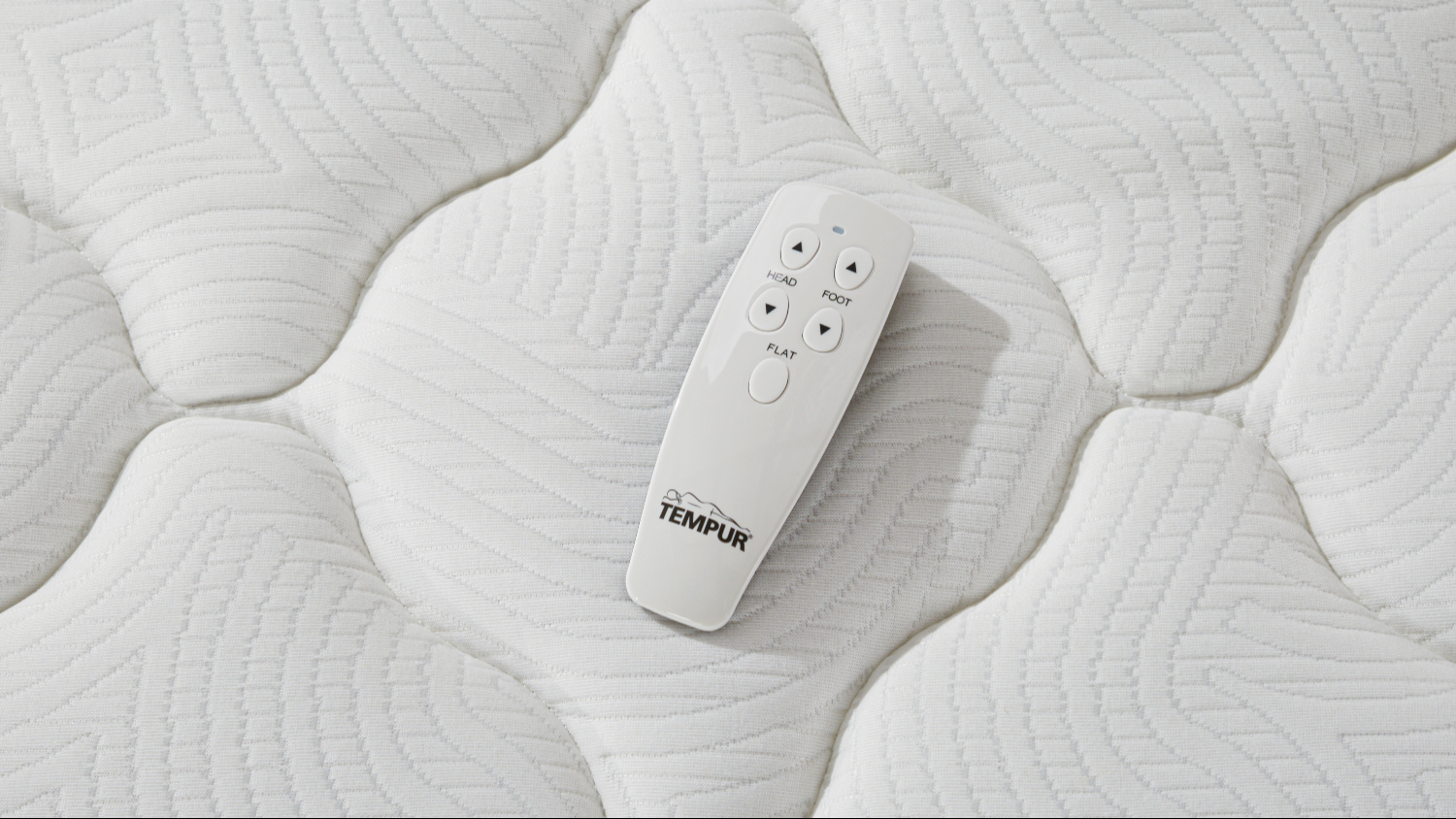 Top‑down close‑up of a white Tempur remote control resting on the mattress surface