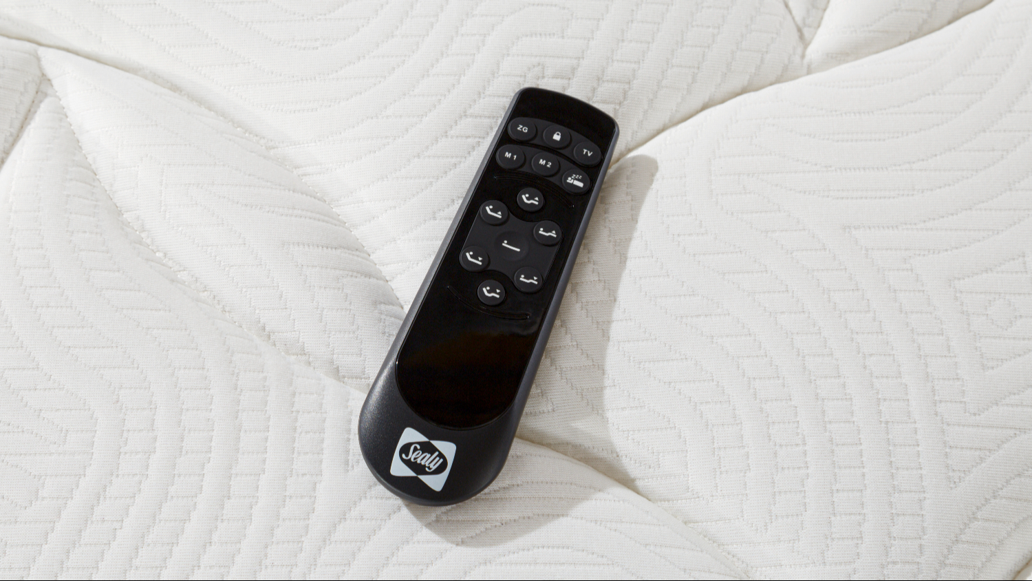 Top‑down close‑up of a black Sealy remote control placed on the white quilted mattress surface