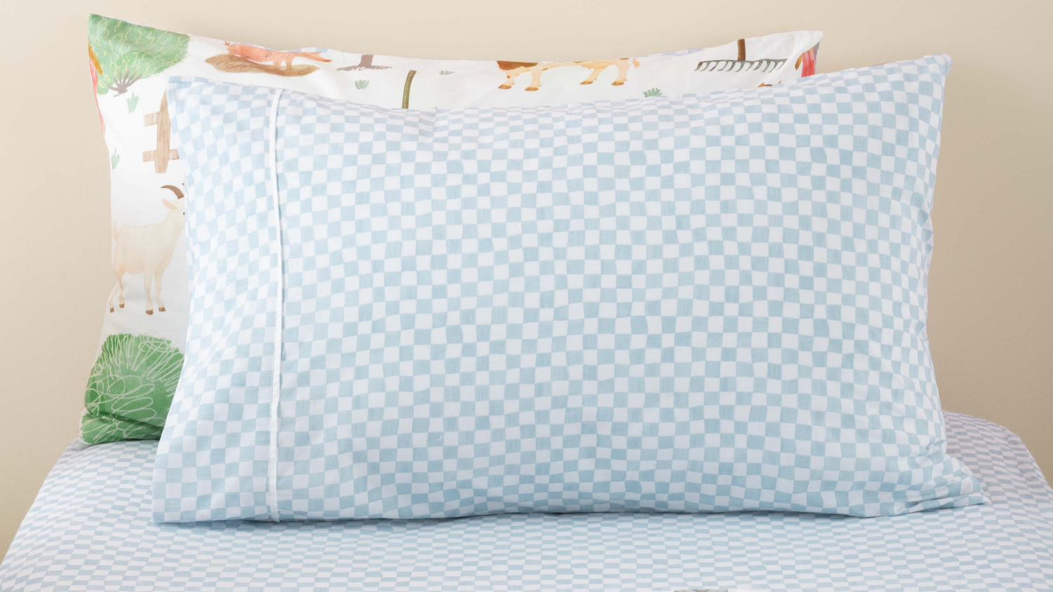 A front-facing view of a pillowcase and fitted sheet set featuring a light blue and white "wavy check" pattern