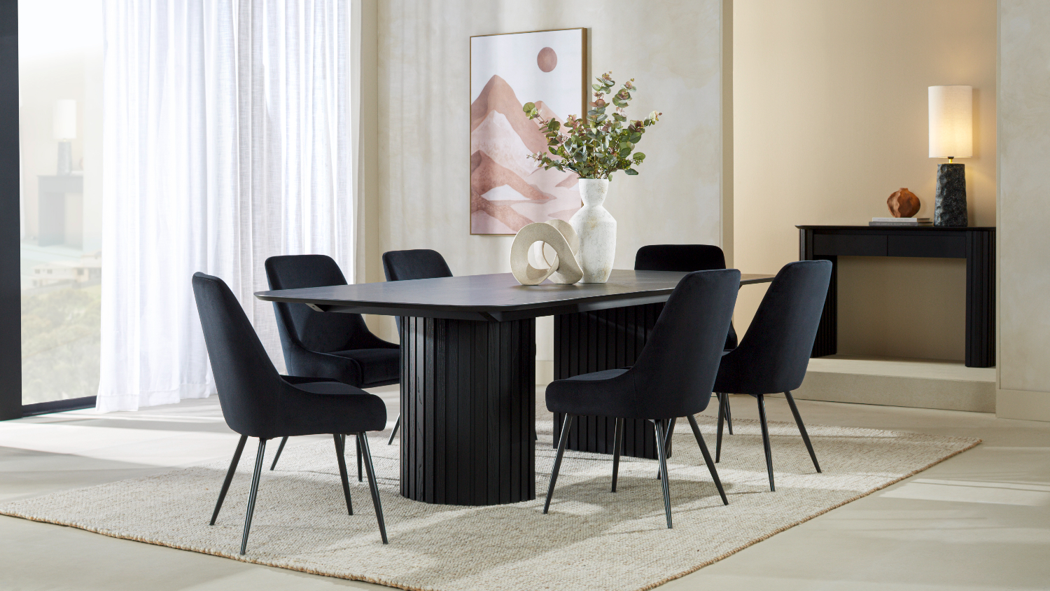 Rectangular black dining table with rounded corners, surrounded by six black upholstered chairs