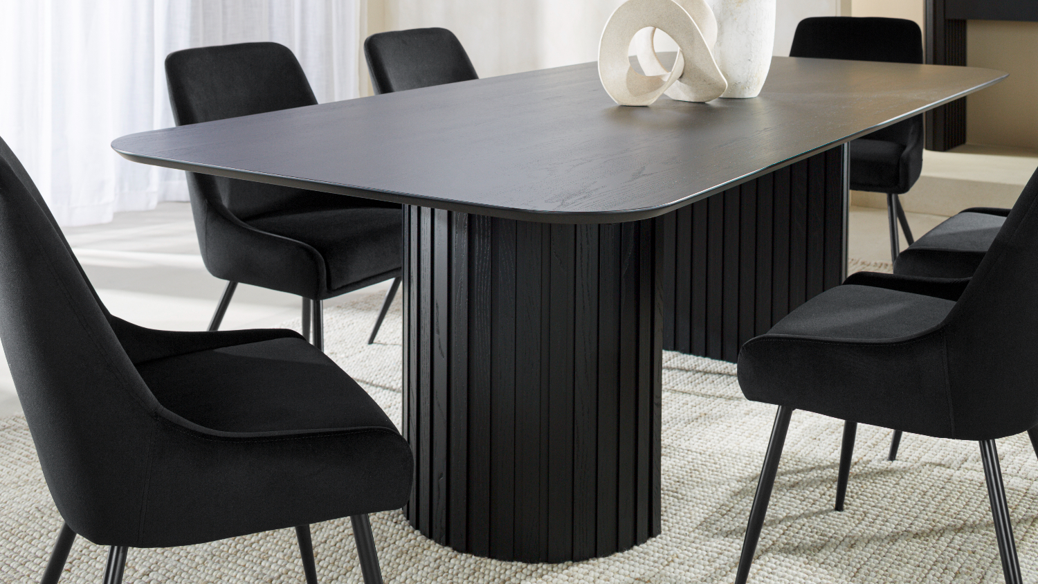 Close-up of the dining table’s black pedestal bases beneath a smooth rectangular top, with upholstered chairs