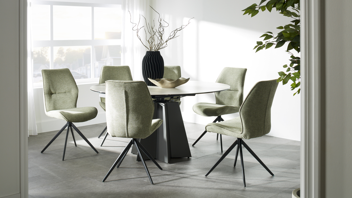 Oval light-top dining table with a black geometric base, surrounded by six olive green upholstered chairs