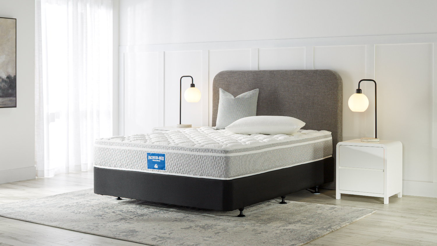 Modern bedroom setup featuring an Incredi‑Bed medium mattress on a dark base with an upholstered headboard and bedside lamps