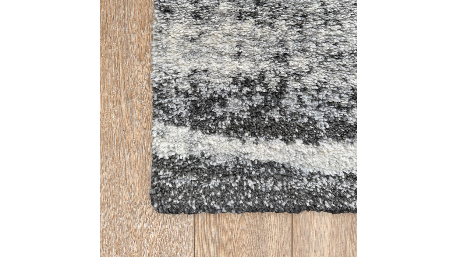 Corner detail of the rug placed on a light wooden floor, showing the thick pile edge and the ombre pattern