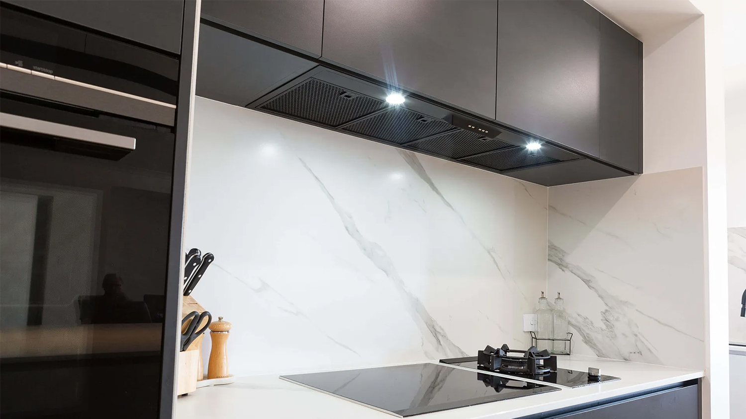 Underside of a black range hood with five mesh filters, two LED lights, and a central control panel