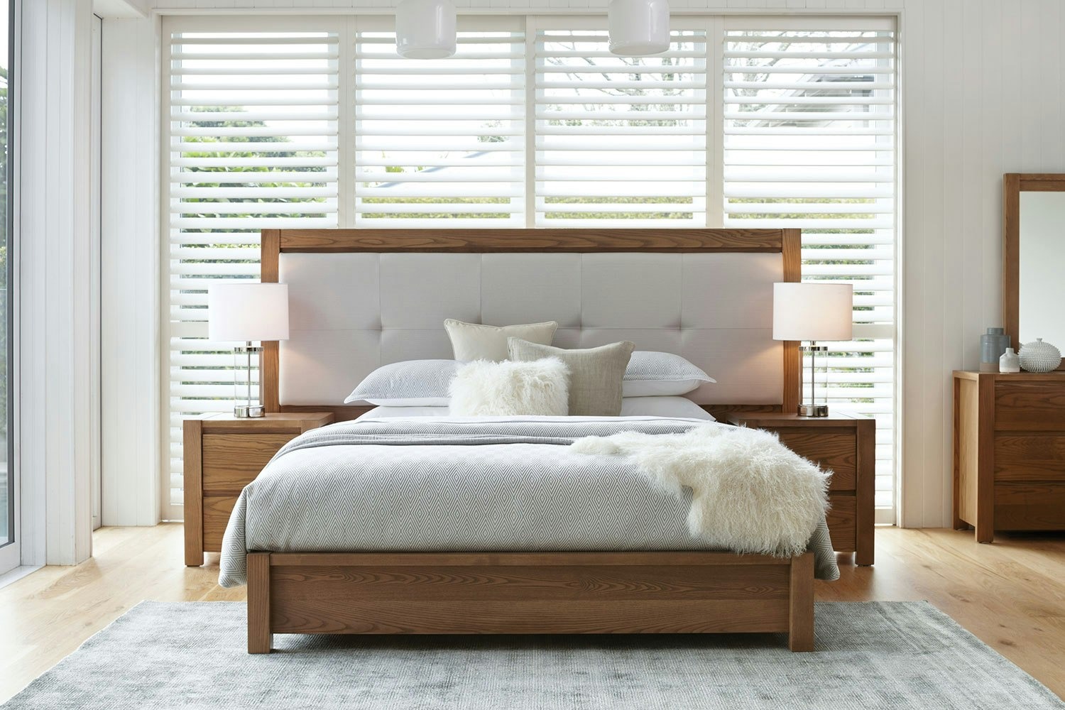 Milford Extended Californian King Bed Frame with wooden bed, white bedding, two lamps, and large windows with blinds