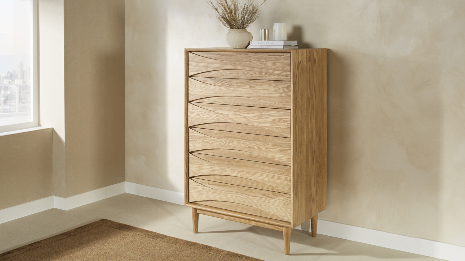 A 6-drawer tallboy featuring distinct carved details on the drawer fronts and tapered wooden legs, styled in a warm beige room next to a window
