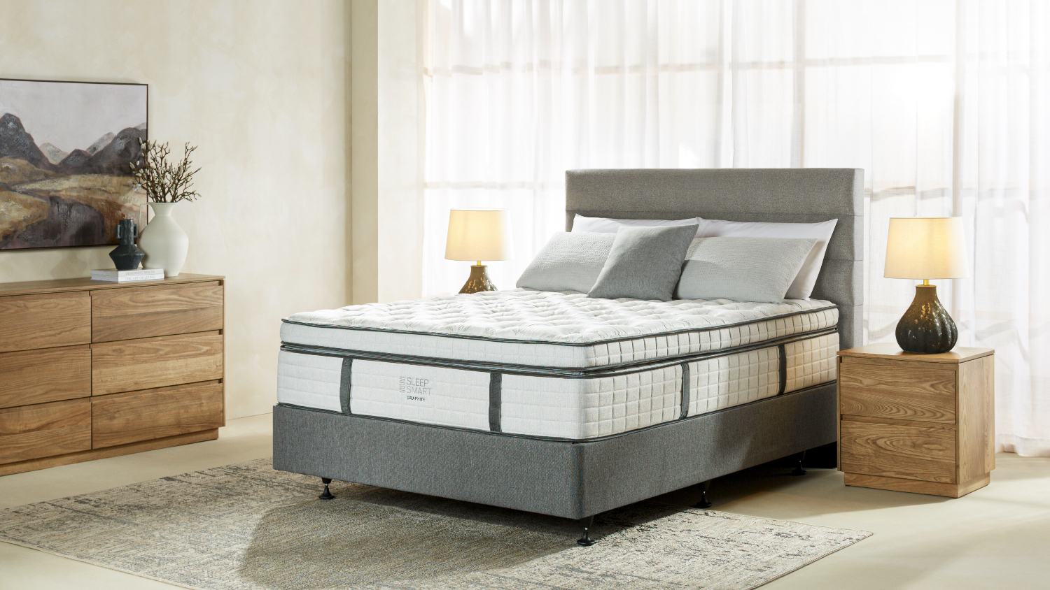 A king-sized Sleep Smart Graphite Soft mattress on an upholstered base in a well-lit bedroom setting
