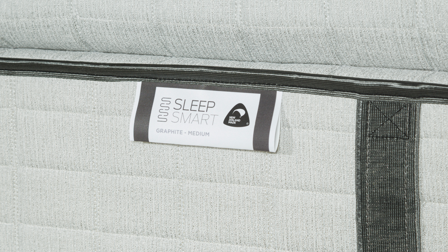 Detailed view of the tag on the mattress reading "Sleep Smart" and "Graphite - Medium”