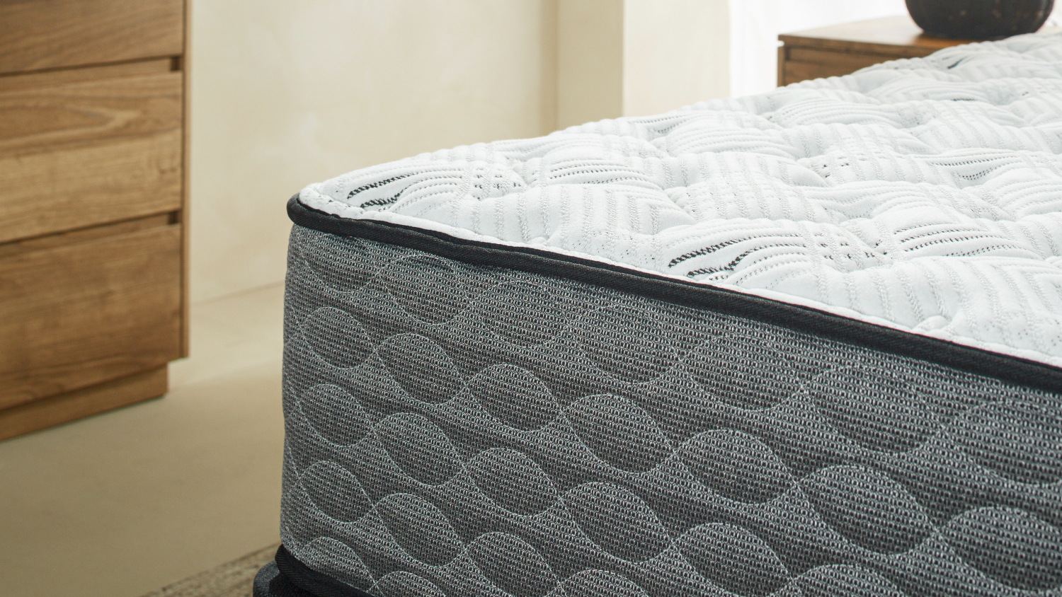 Close-up of a Serene mattress corner with a white quilted top surface and a dark grey, wave-patterned textured side fabric