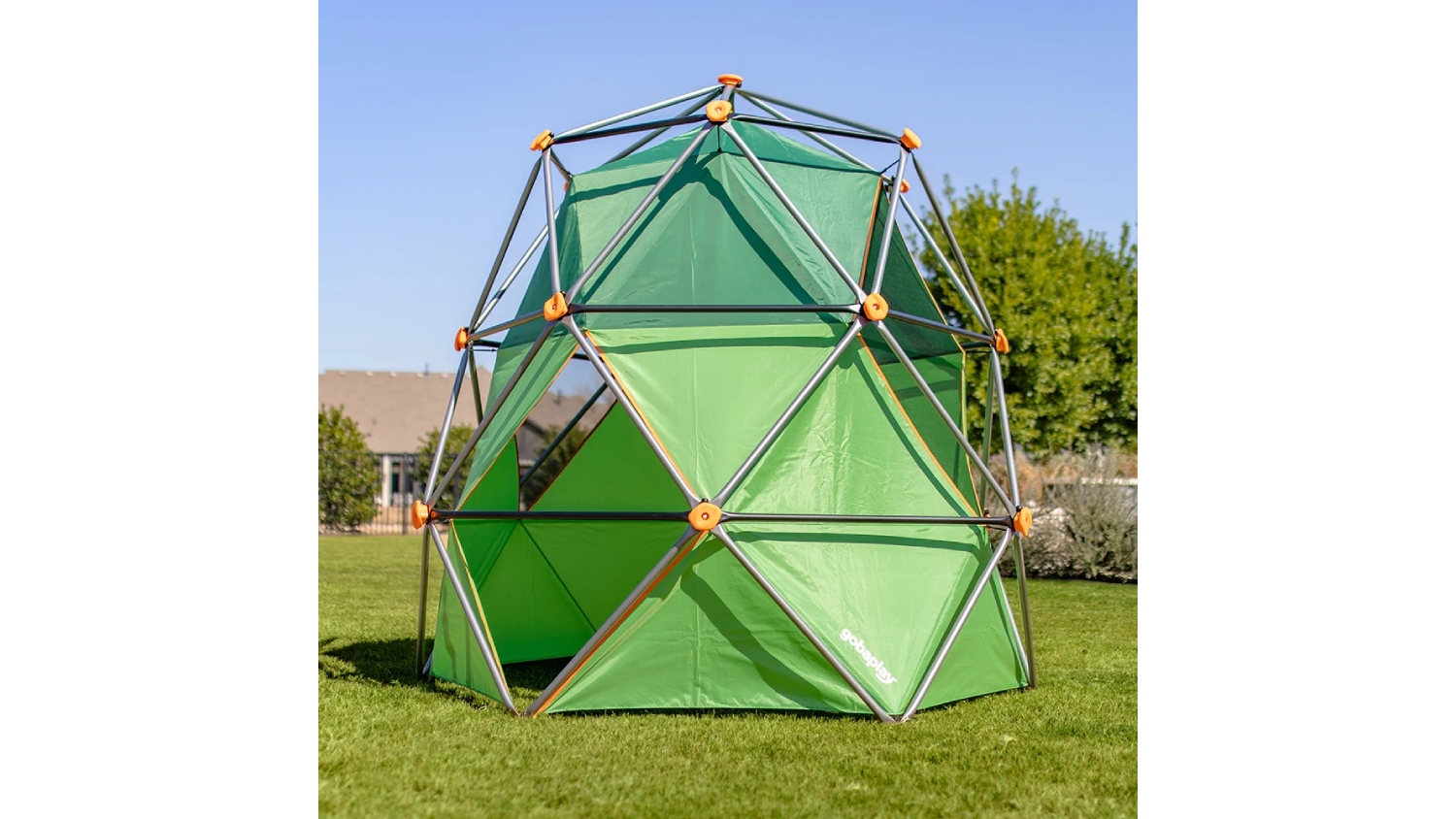 Green Gobaplay SummitPro outdoor climbing dome with a tent, featuring a metal frame and orange joints, set on a grassy lawn under a clear blue sky