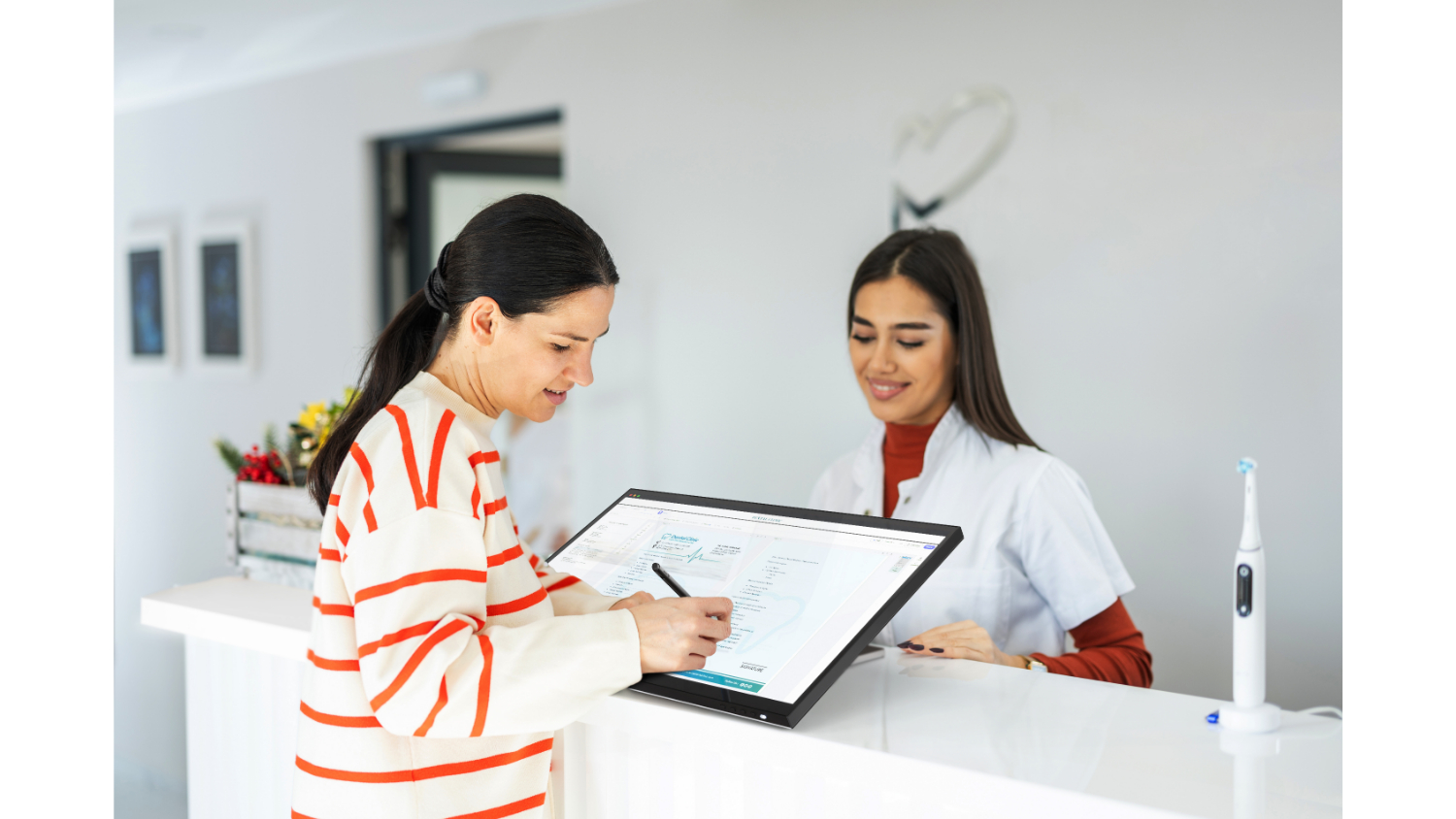 A woman signing a document on the Alogic monitor at a clinic reception desk