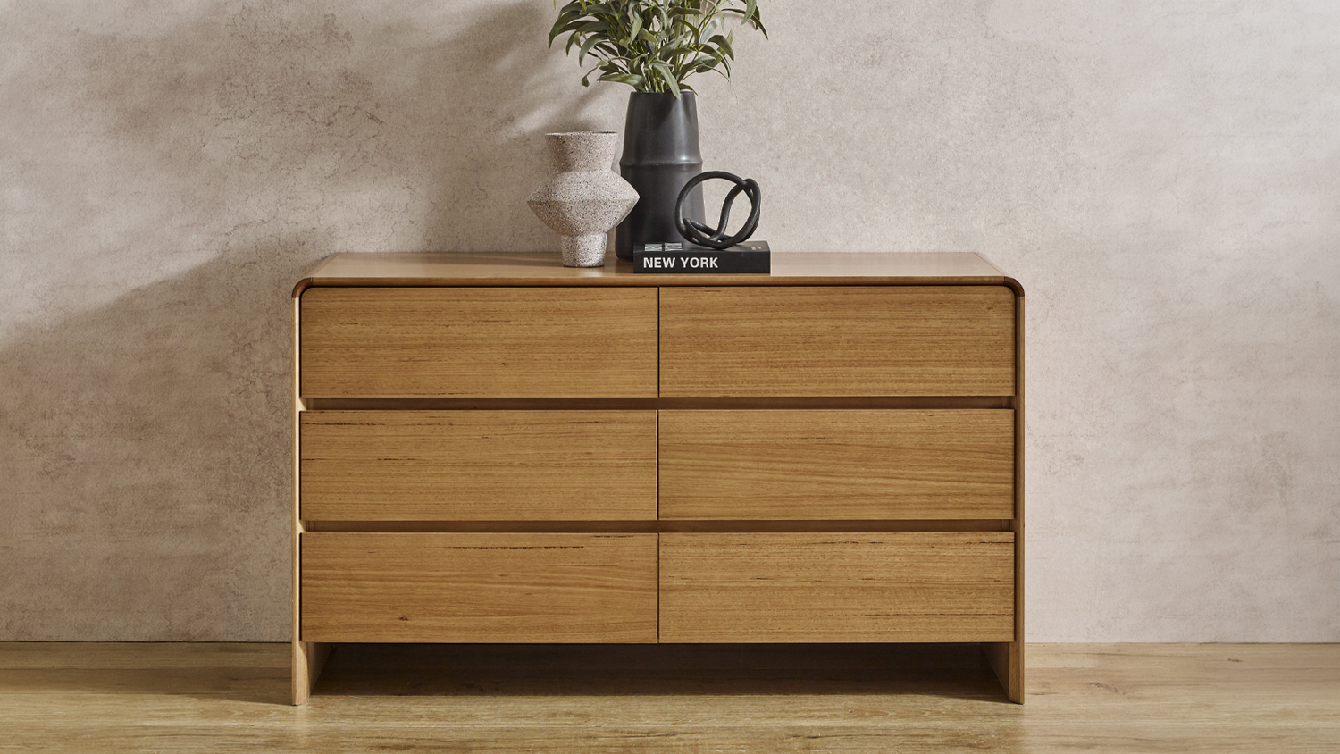 Front view of the Cassie 6-drawer wooden dresser against a textured wall with decor on top