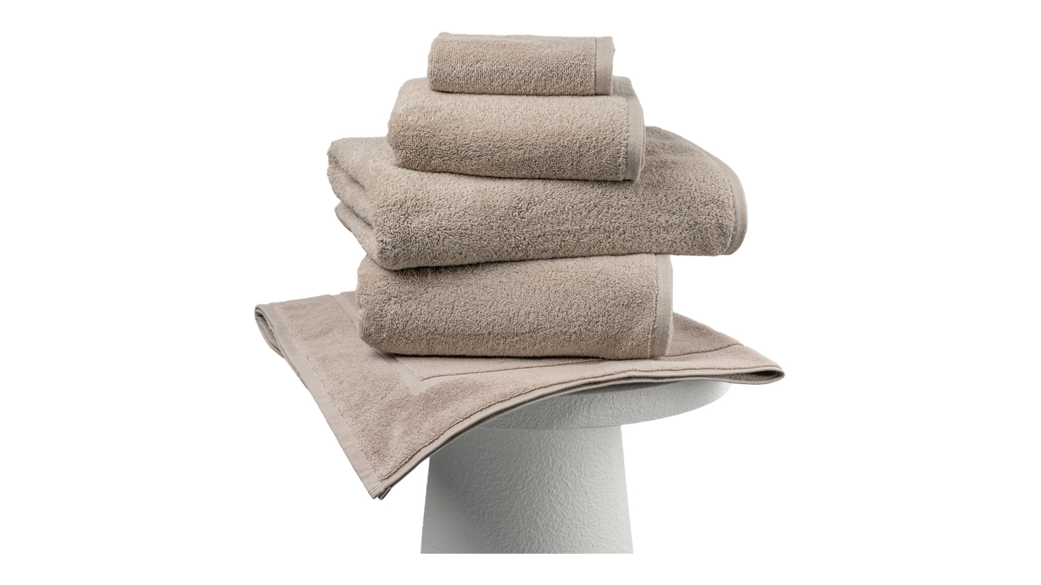 Stack of plush Natural Baksana Bursa Turkish-style towels and a white bath mat neatly displayed on a pedestal