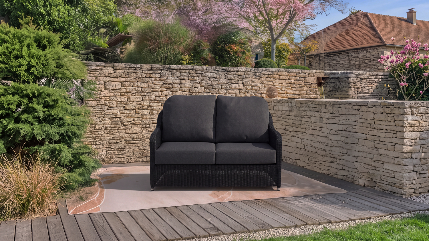 Marbella 2 Seater Outdoor Sofa positioned on a patio deck within a landscaped garden