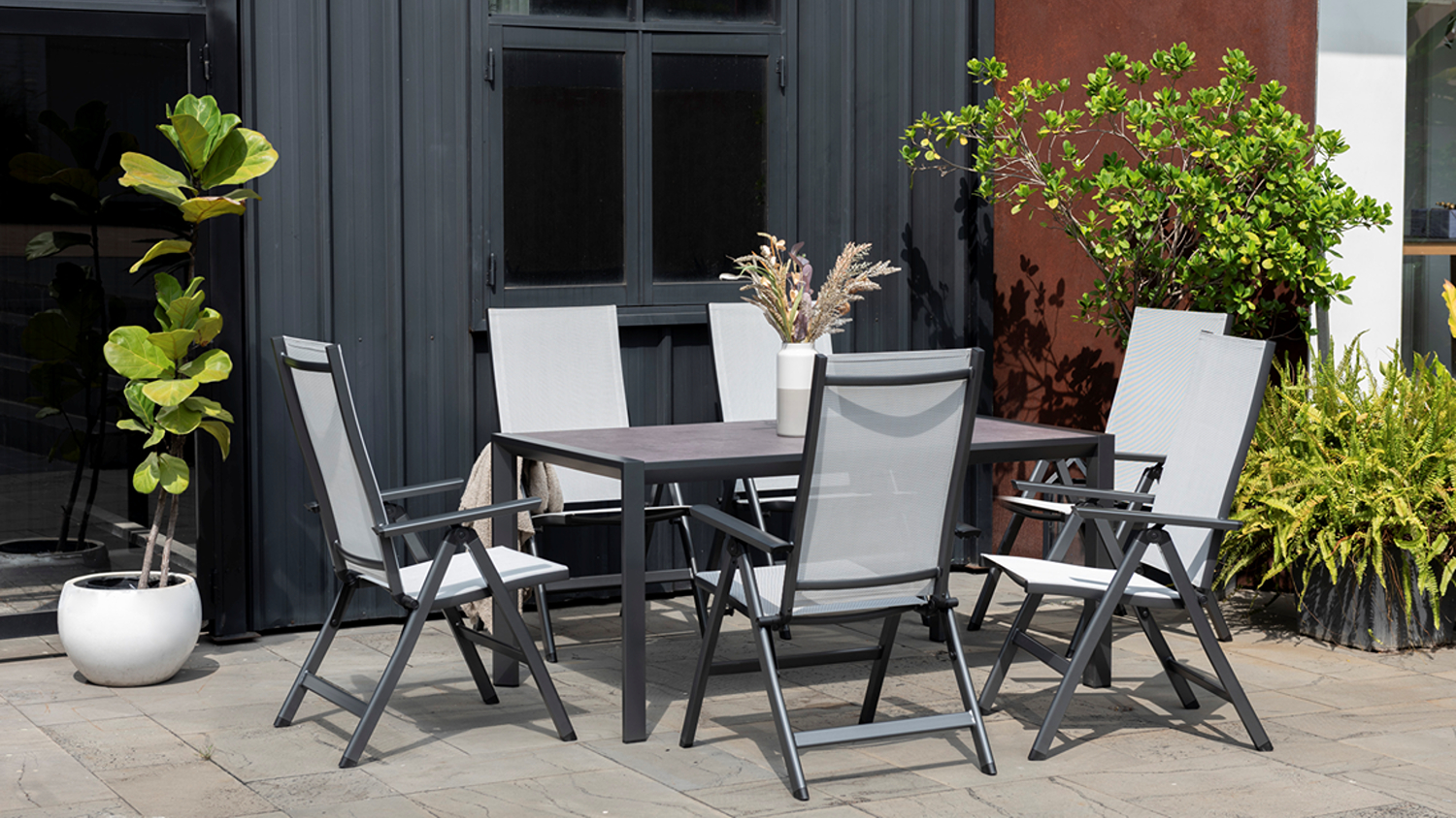 Urbanite 7 Piece Outdoor Dining Suite arranged on a patio, featuring a rectangular table surrounded by six chairs