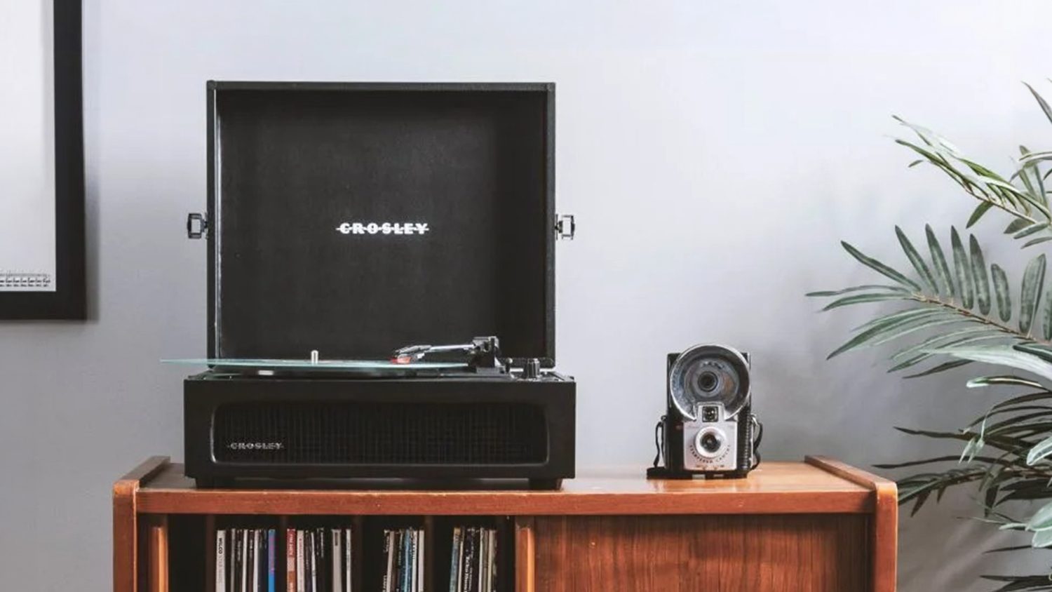 Black suitcase-style turntable displayed on a wooden cabinet with a vinyl record