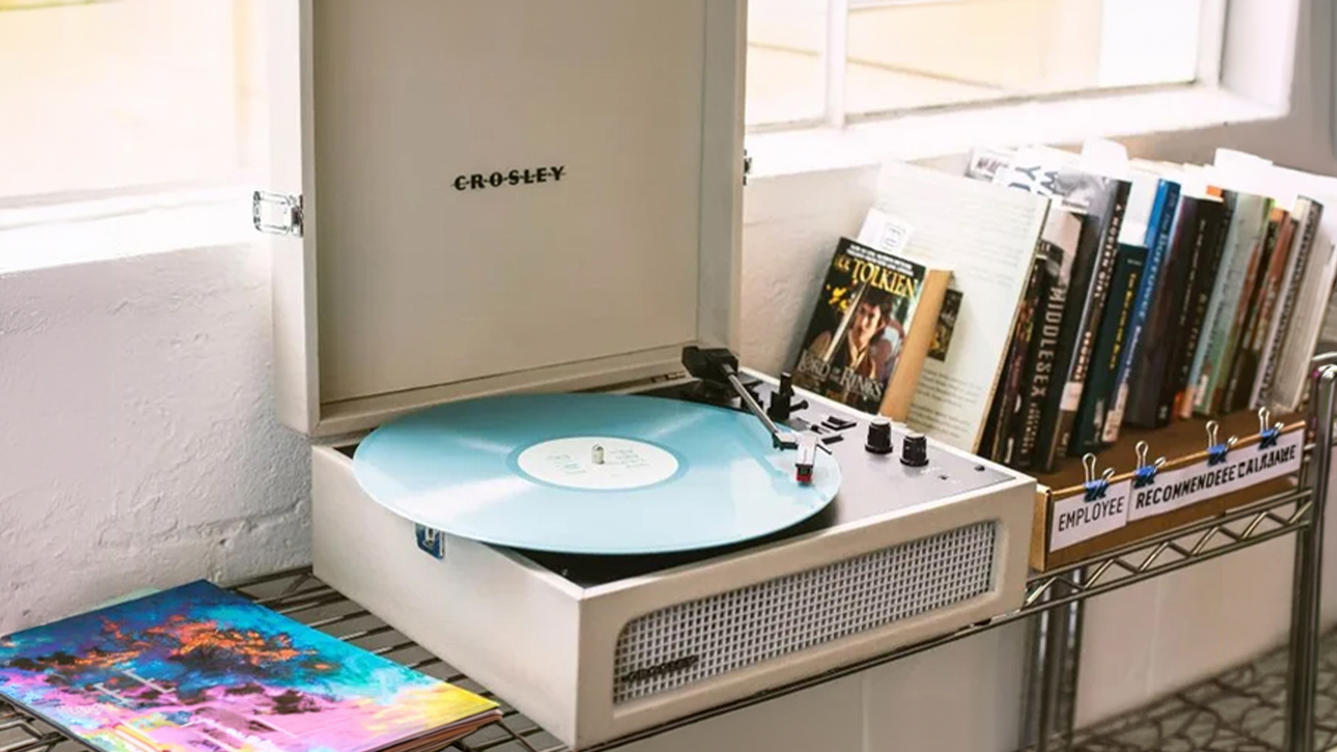 Cream suitcase-style turntable playing a light blue vinyl record on a metal shelf