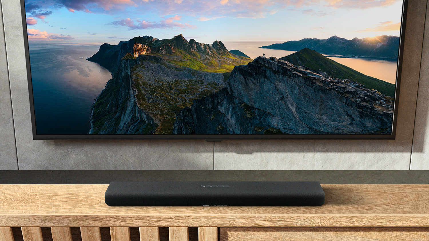 Black Yamaha soundbar positioned beneath a wall-mounted TV displaying a mountain landscape