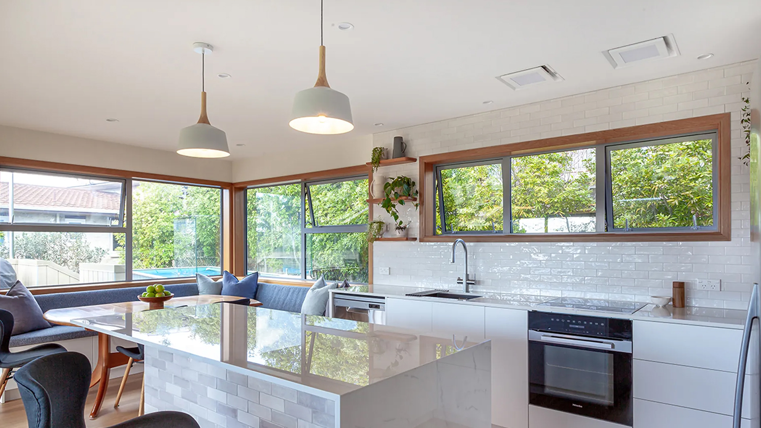 Modern kitchen island and cooktop area with twin ceiling rangehood modules above