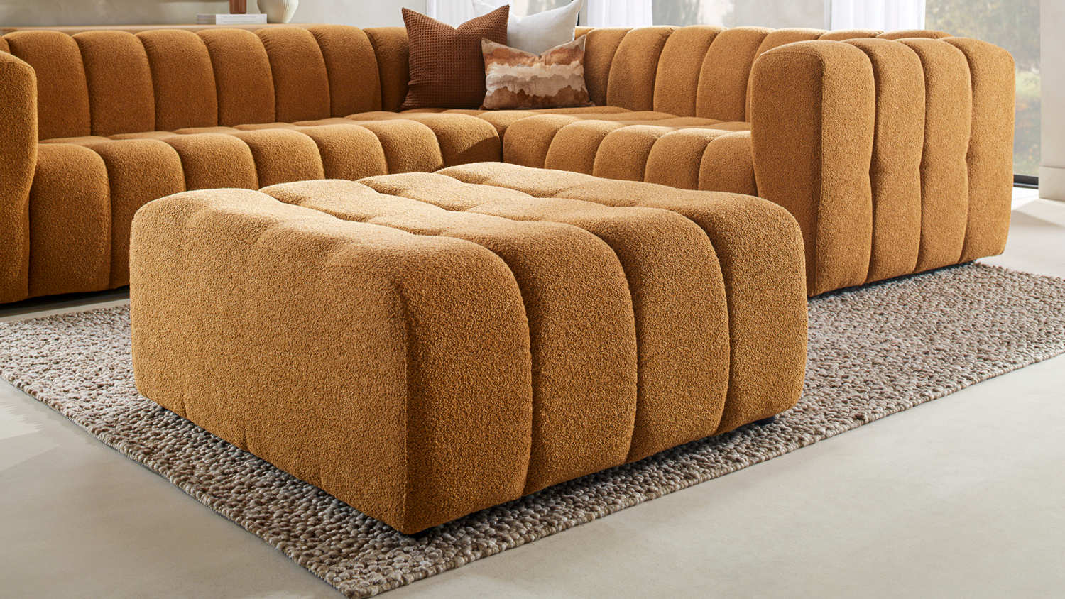 Louisiana Fabric Modular Ottoman placed on a textured rug in front of a matching sectional couch