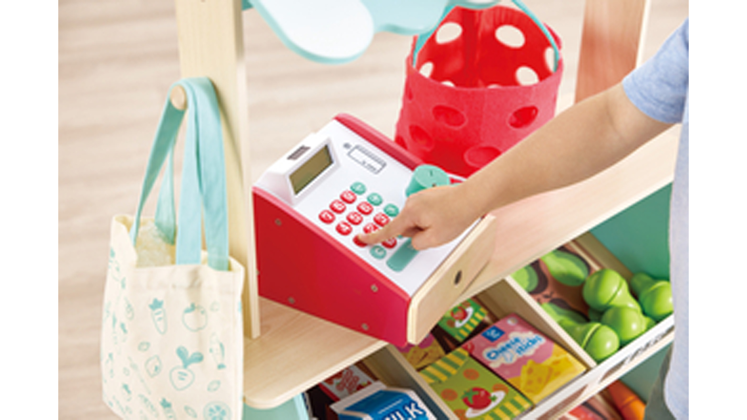 Close-up of the market stall counter with toy cash register, shopping bag, and pretend fruit and vegetables