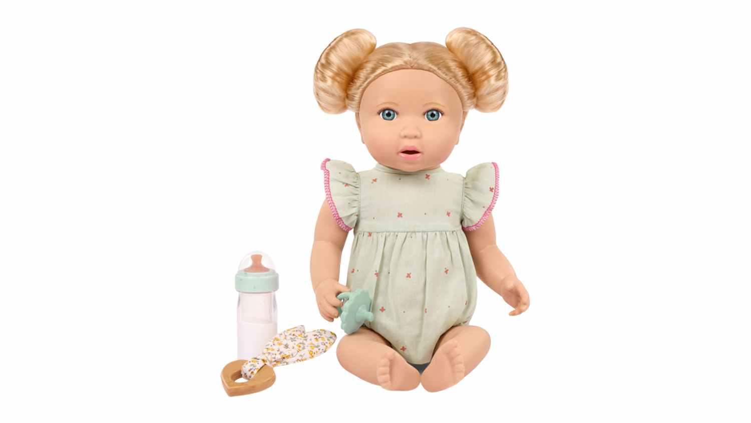 A blonde LullaBaby 14-inch doll with hair buns, wearing a sage green romper, sits next to a toy bottle and a pacifier